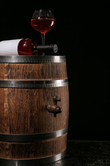 Wooden barrel with bottle and glass of wine on dark background