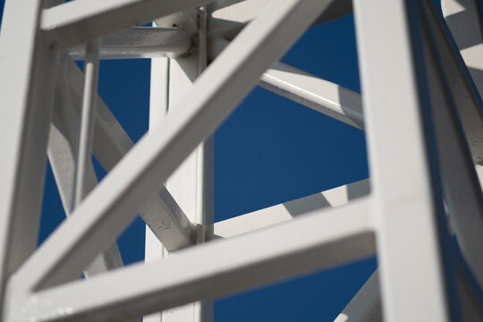 The cross bracing on a steel tower, with beams at diagonals to reinforce the structure. The overall design has a sense of geometry and patterning. The background is a clear blue sky.