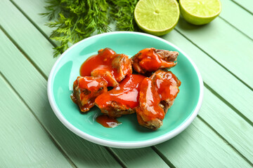 Plate with canned fish in tomato sauce, lime and dill on green wooden table