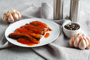 Plate with canned fish in tomato sauce on grey table