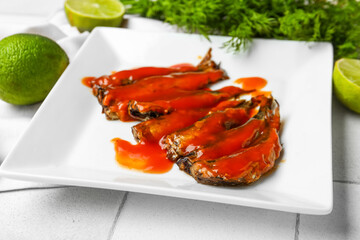 Plate with canned fish in tomato sauce, lime and dill on white tiled table
