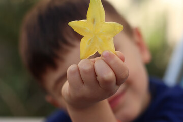Menino mostra na sua mão uma estrela, formada pela fatia de uma carambola
