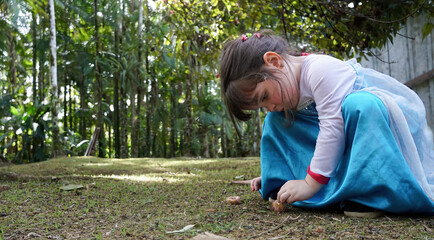Criança, menina, brincando sózinha com terra, junto à natureza, vestindo fantasia de princesa
