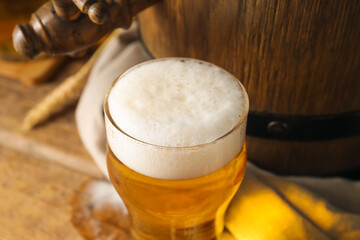Glass of cold beer and oak barrel on wooden background, closeup