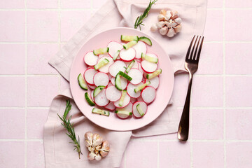 Plate with fresh slices of radish and cucumber on pink tile background