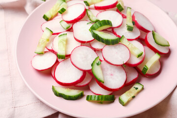 Plate with fresh slices of radish and cucumber on pink tile background