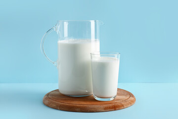 Jug and glass with fresh milk on blue background