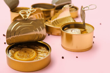 Opened tin cans with different fish on pink background
