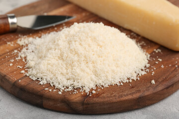 Wooden board with tasty grated Parmesan cheese on grunge background, closeup