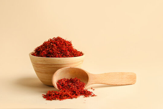Wooden bowl and spoon with pile of saffron on light background