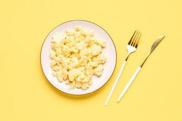 Plate of tasty scrambled eggs and cutlery on yellow background