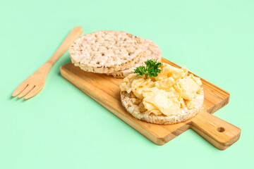 Wooden board with tasty scrambled eggs and rice crackers on green background