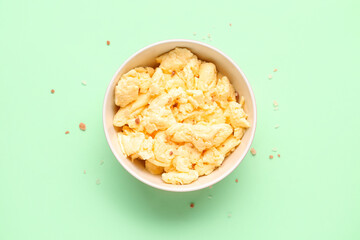 Bowl of delicious scrambled eggs on green background