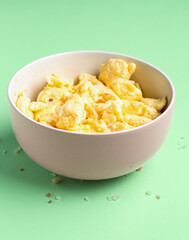 Bowl of delicious scrambled eggs on green background, closeup