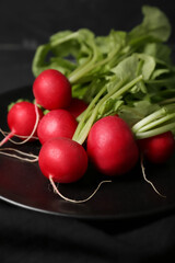 Plate of ripe radish with green leaves on dark background, closeup