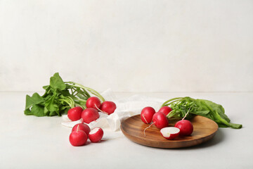 Plate of ripe radish with green leaves on light background