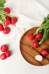 Plate of ripe radish with green leaves on light background