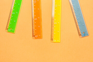 Colorful plastic rulers on orange background