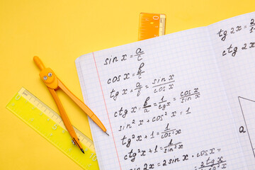 Copybook with maths formulas and stationery on yellow background