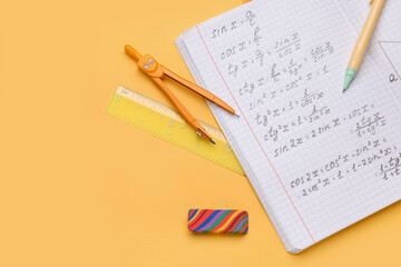 Copybook with maths formulas and stationery on orange background