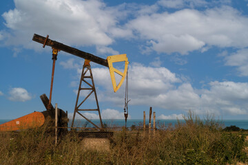 Naklejka premium A small oil pump, an energy industrial oil machine, in the agricultural field in Bulgaria. In the background is the Black Sea