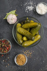 Bowl with tasty fermented cucumbers and ingredients on dark grunge background