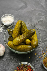 Bowl with tasty fermented cucumbers and ingredients on dark grunge background