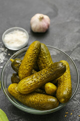 Bowl with tasty fermented cucumbers and ingredients on dark grunge background