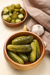 Bowl with tasty fermented cucumbers on light wooden background
