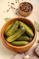 Bowl with tasty fermented cucumbers on light wooden background