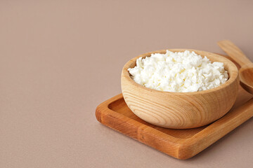 Bowl with tasty cottage cheese on beige background