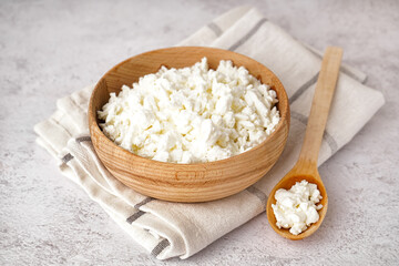 Bowl and spoon with tasty cottage cheese on light grunge background