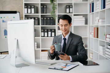 Young handsome man typing on tablet and laptop while sitting at the working wooden table modern office