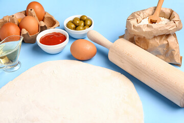 Raw dough and ingredients for preparing vegetable pie on blue background
