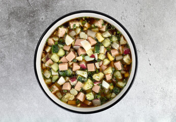 Traditional russian soup - okroshka with vegetables, sausages and kvass. Russian cold summer soup on gray table. Top view. 