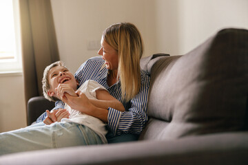 Mother and son plays tickle at home on the sofa living room. Happy motherhood and childhood