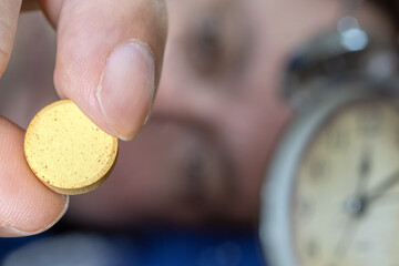 A man lying in bed takes a pill after midnight, close up