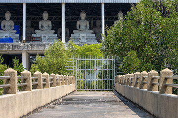 A locked gate on the way to a building with statues of a seated Buddha in a Buddhist monastery complex, Thailand