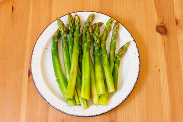 Green boiled asparagus in a plate on a wooden table