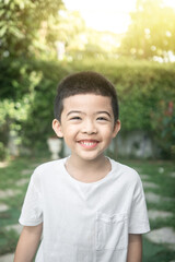 A portrait of an Asian boy. He's smiling. He's wearing a white shirt. green tree background