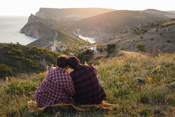 Travelers watch the sunset in the mountains.The couple meets the sunset in the mountains. Two travelers are sitting on the edge of a cliff and admiring the beautiful sunset. Panoramic view.