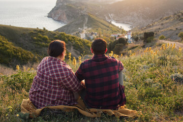 Travelers watch the sunset in the mountains.The couple meets the sunset in the mountains. Two travelers are sitting on the edge of a cliff and admiring the beautiful sunset. Panoramic view.