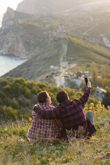 Travelers watch the sunset in the mountains.The couple meets the sunset in the mountains. Two travelers are sitting on the edge of a cliff and admiring the beautiful sunset. Panoramic view.