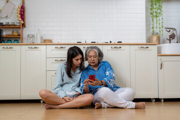 Happy senior woman smiling and sharing data on smartphone with young daughter while sitting on couch at home together.
