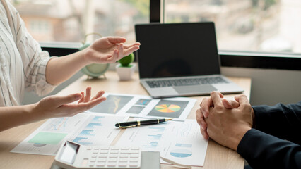 Two business people sitting at workplace and discussing about earnings on a graph to plan investments.