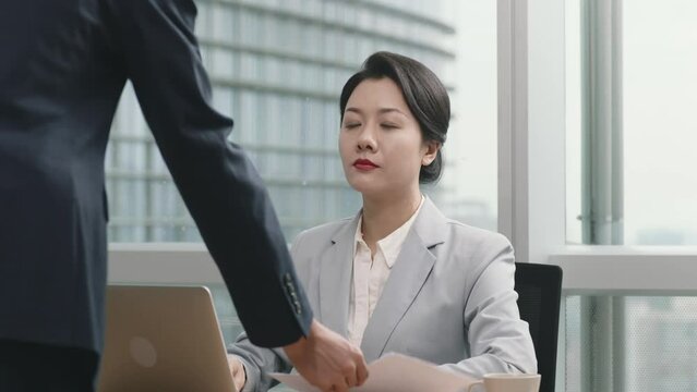 asian manager reviewing and signing in office a document presented by female assistant 