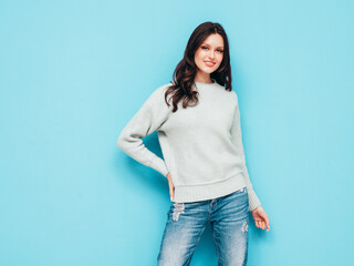 Young beautiful smiling female in trendy summer jeans and warm winter sweater clothes. Sexy carefree woman posing near blue wall in studio. Positive model. Cheerful and happy. Isolated.