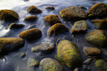 Fototapeta premium Rocks and pebbles on a tropical beach in the Caribbean sea. Surf water motion with longtime exposure showing flowing streams and rivulets. Natural background with low contrasting evening sun light.