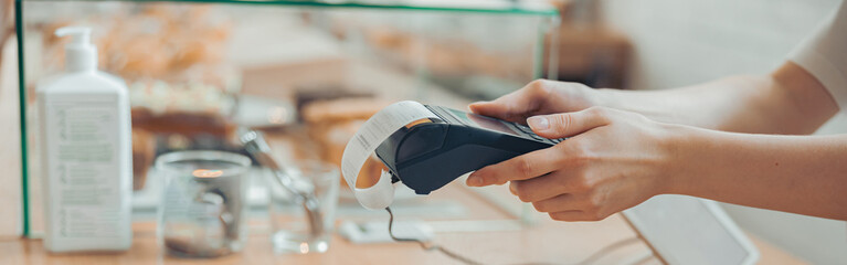 Female barista using terminal for contactless payment in cafeteria