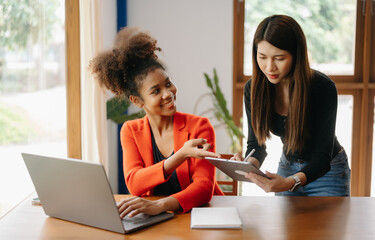 Two Asian businesswoman discuss investment project working and planning strategy with tablet laptop computer in modern office.